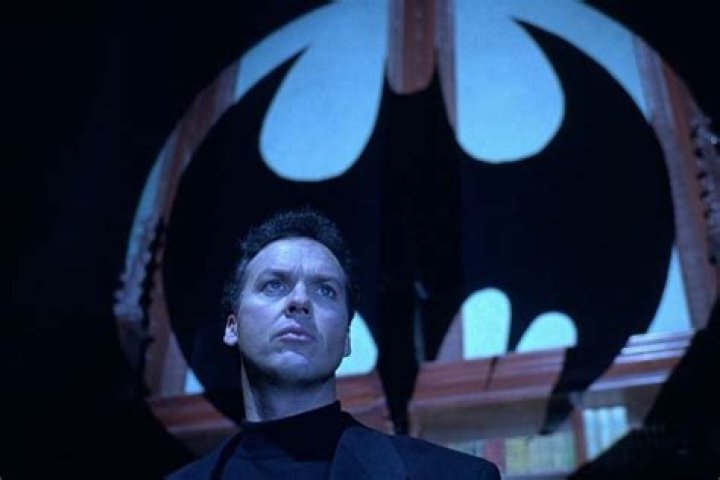 Bruce Wayne (Michael Keaton) standing in front of a silhouette of the bat signal in Batman Returns.